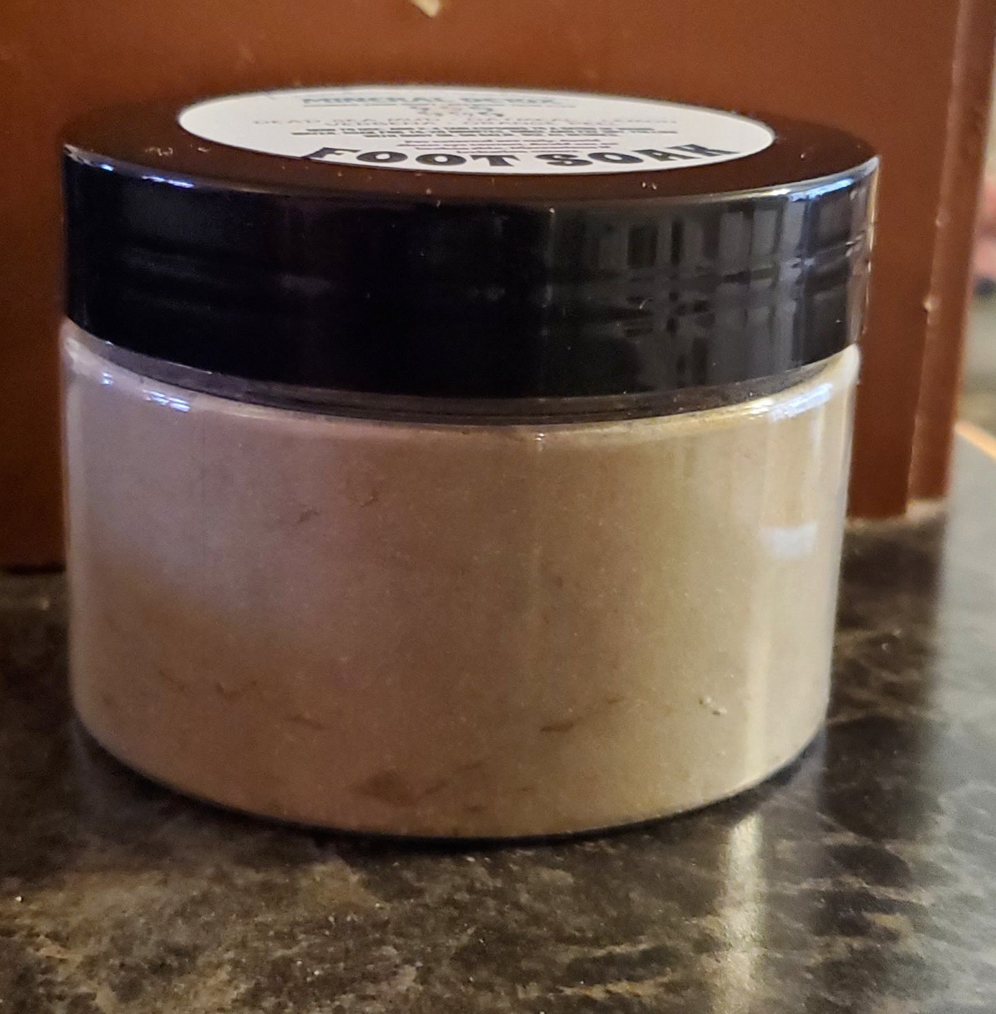 Jar of foot soak on a marble surface with a brown background
