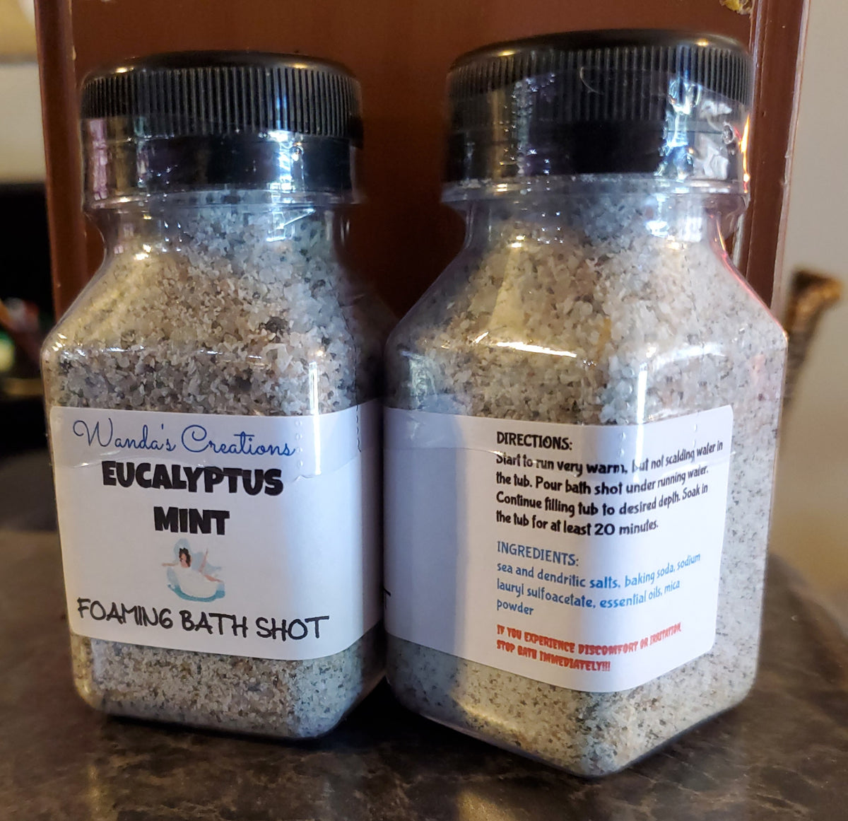 Two glass jars with labels containing directions for making a Eucalyptus Mint Foaming Bath Shot, one jar labeled 'Eucalyptus Mint' and the other with 'FOAMING BATH SHOT' text. Both jars have white and blue labels with additional text.