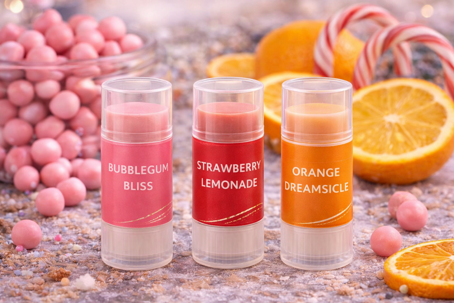 Three lip balm tubes labeled 'Bubblegum Bliss', 'Strawberry Lemonade', and 'Orange Dreamsicle' with candy and fruit in the background.