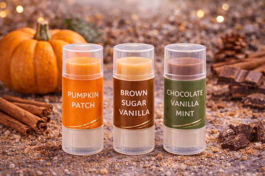 Three lip balm tubes labeled 'Pumpkin Patch', 'Brown Sugar Vanilla', and 'Chocolate Vanilla Mint' on a rustic background with pumpkins and cinnamon sticks.