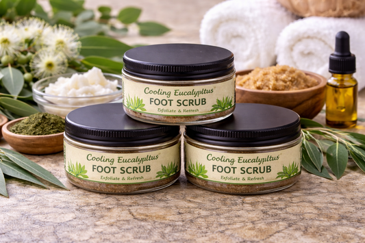 Three jars of Cooling Eucalyptus Foot Scrub on a stone surface with eucalyptus leaves and flowers.