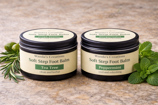 Two jars of Wanda's Creations Soft Step Foot Balm with labels for Tea Tree and Peppermint scents on a stone surface.